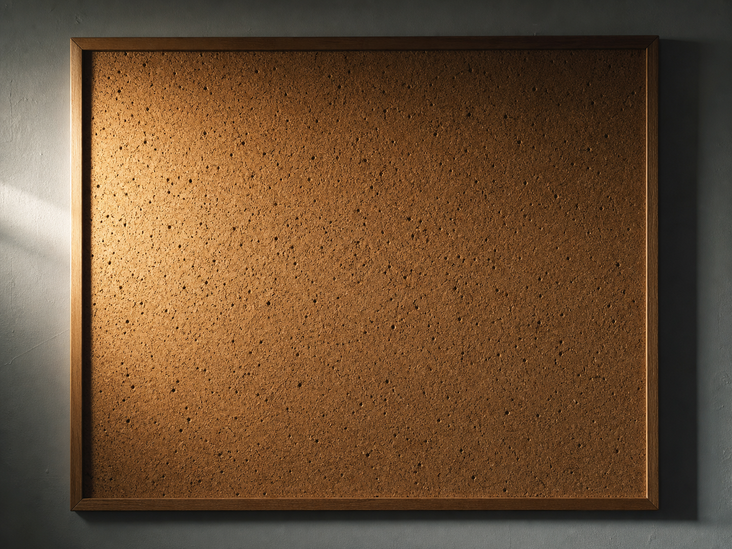 Un panneau d’affichage en liège entièrement vide, criblé de trous de punaises, sous une lumière latérale qui creuse chaque perforation.